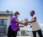 Home Two African women wearing masks deliver a package outdoors, practicing safety.